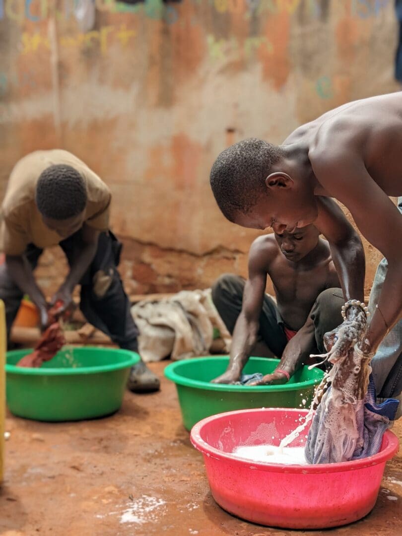 A group of young men washing dishes in green bowls.