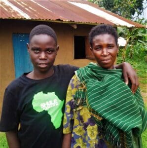 A mother and son stand outside their home.